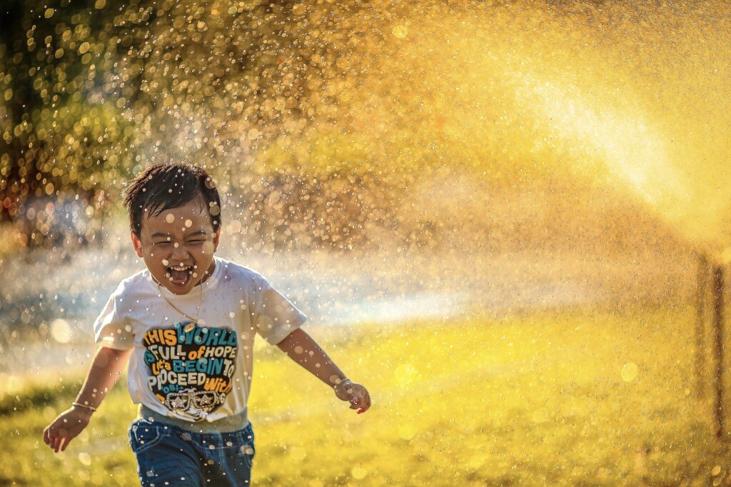 Een jongetje dat blij door een sproeier heen rent.