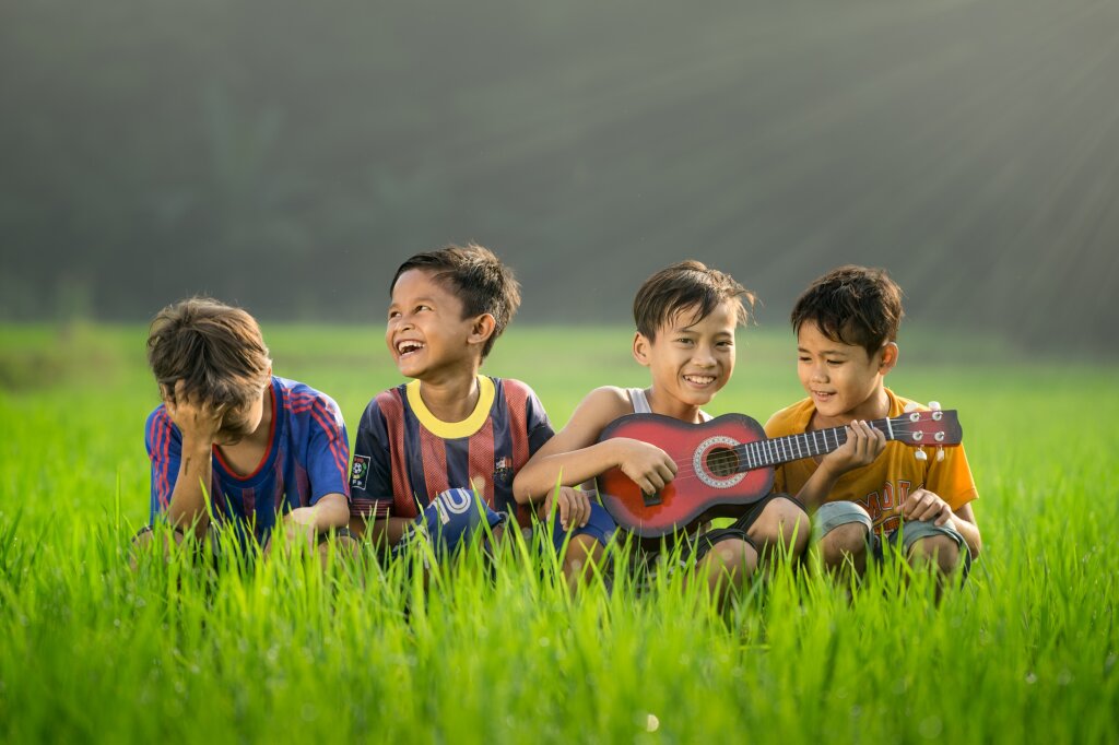 Vier vrolijke jongens in het gras. Voetbalshirts, met gitaar.